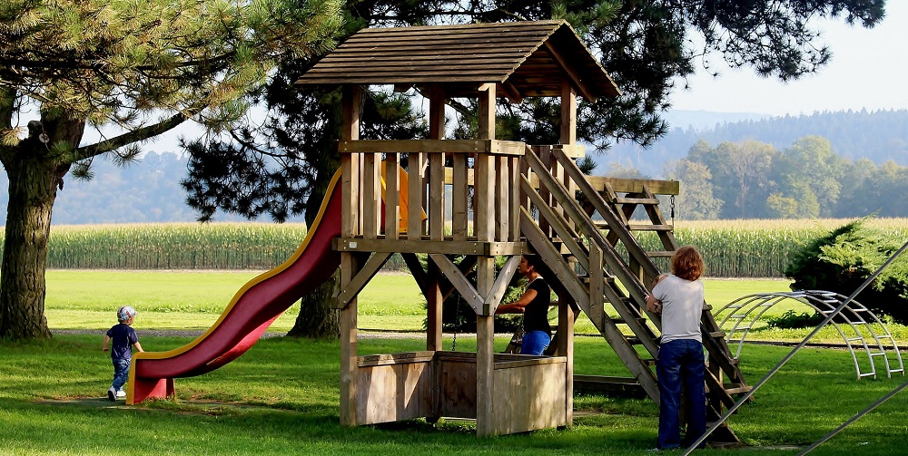 An image of parents and children around a playset with a slide on it.