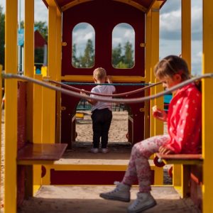 An image showing 2 children playing on a playset in park.
