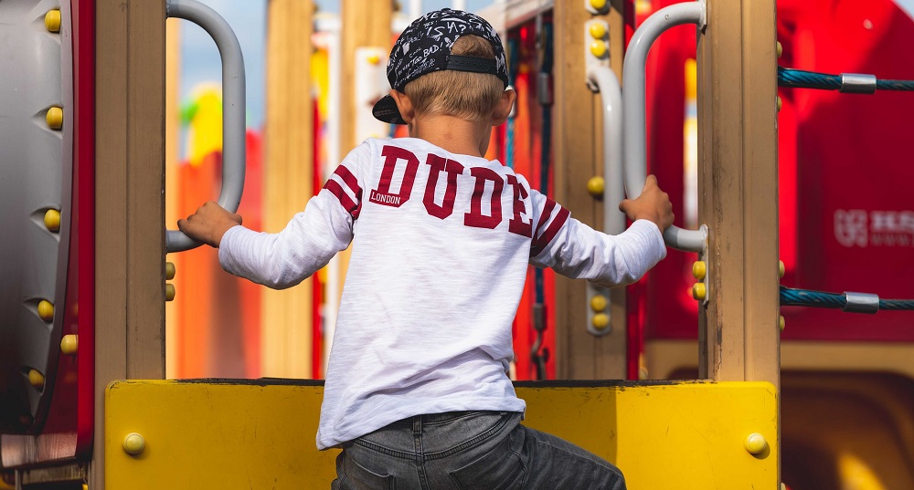 An image of a child climbing a playset with a shirt that reads, "DUDE".