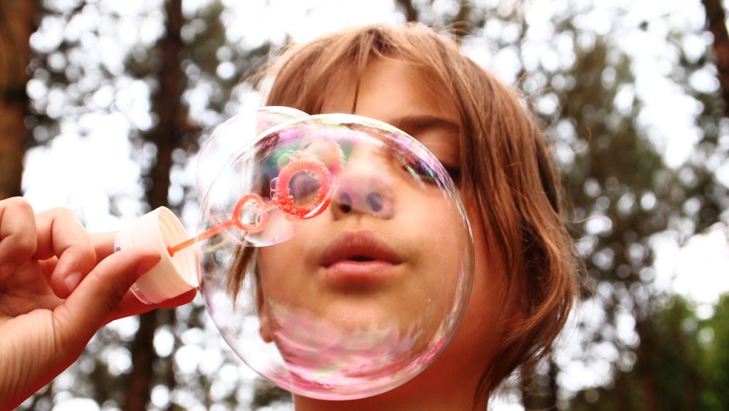An image that shows a child blowing bubbles.