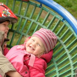 An image of two children playing on a basket swing seat.