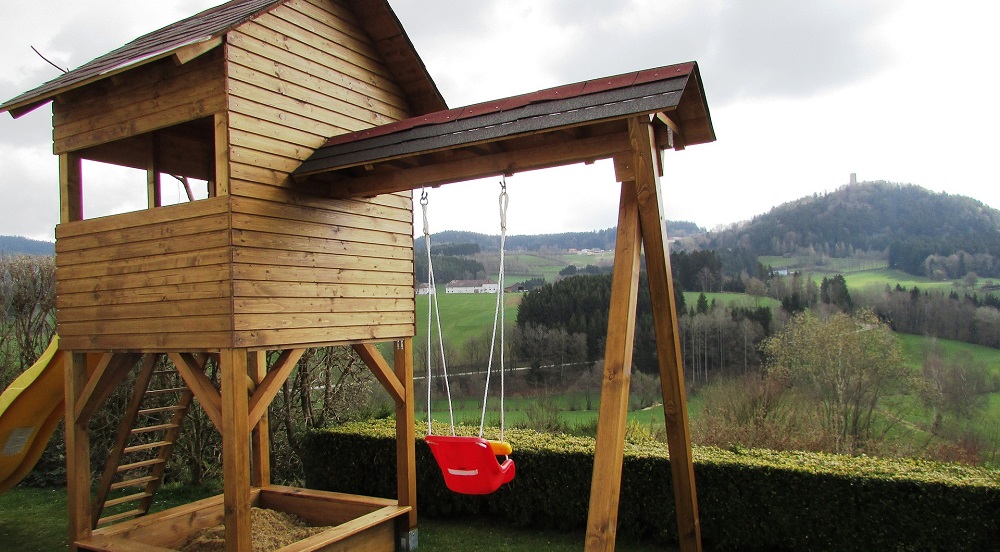 An image of a wooden playset with a treeline in the background.