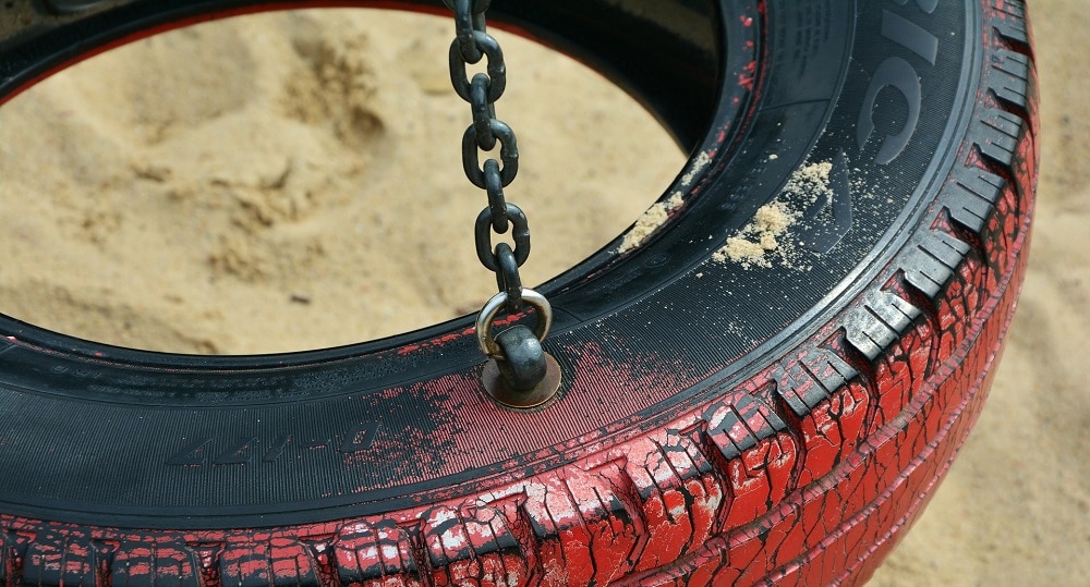 An image of a black tire swing that is painted red and attached to a swing set.