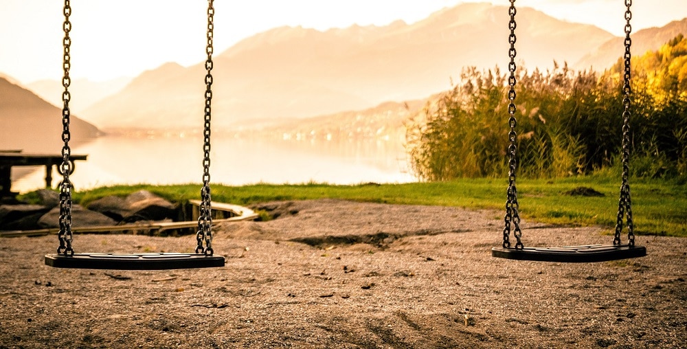 An image of a playset with two swing seats on a beach.