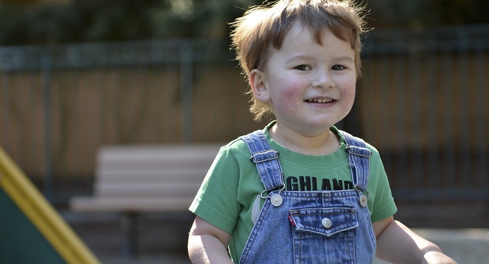An image showing a young child smiling in a park.