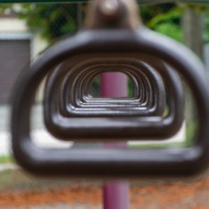 An image showing an artistic shot of a view of a park through a few trapeze d-rings.