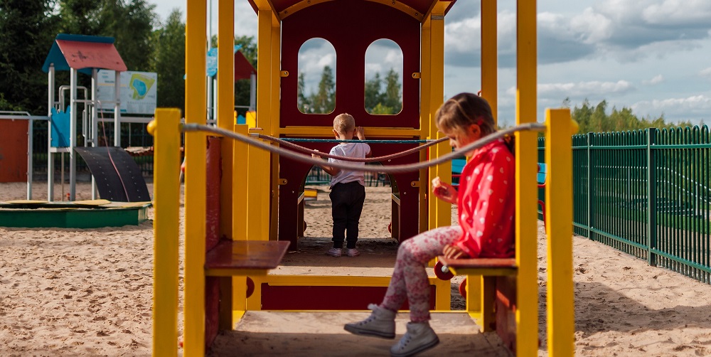 An image showing 2 children playing on a playset in park.