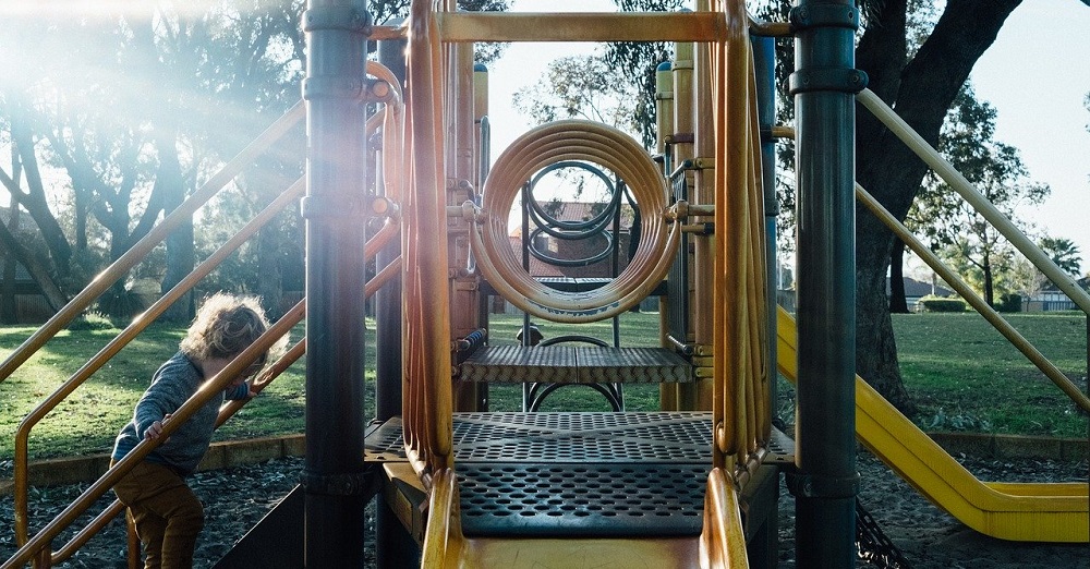 An image of a child climbing the steps of a playset in a park.