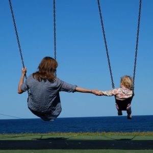 An image showing a woman holding a child's hand while swinging from a swing set.
