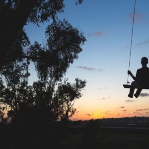 An image of a child on a flat swing seat with the sun setting in front of them.