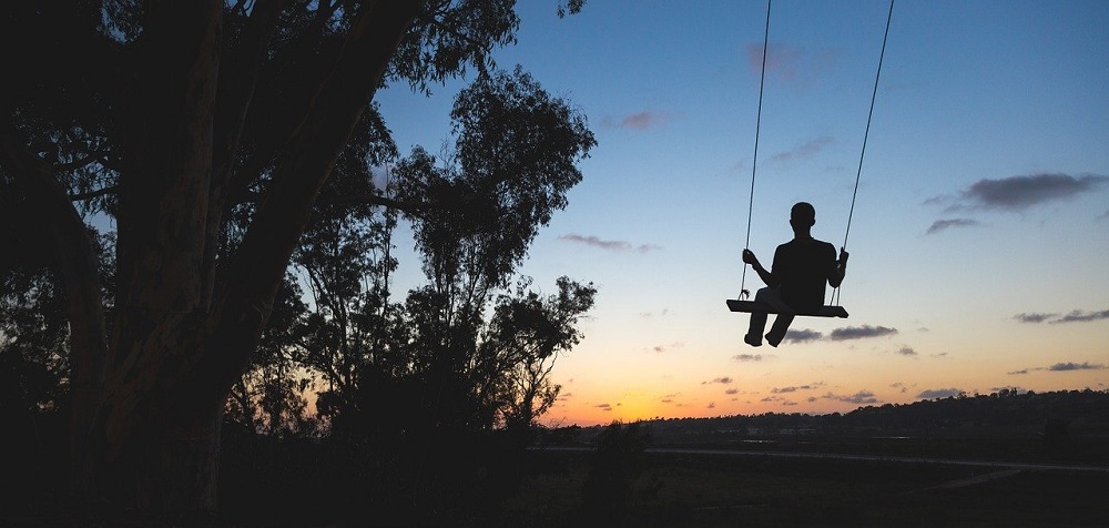 An image of a child on a flat swing seat with the sun setting in front of them.