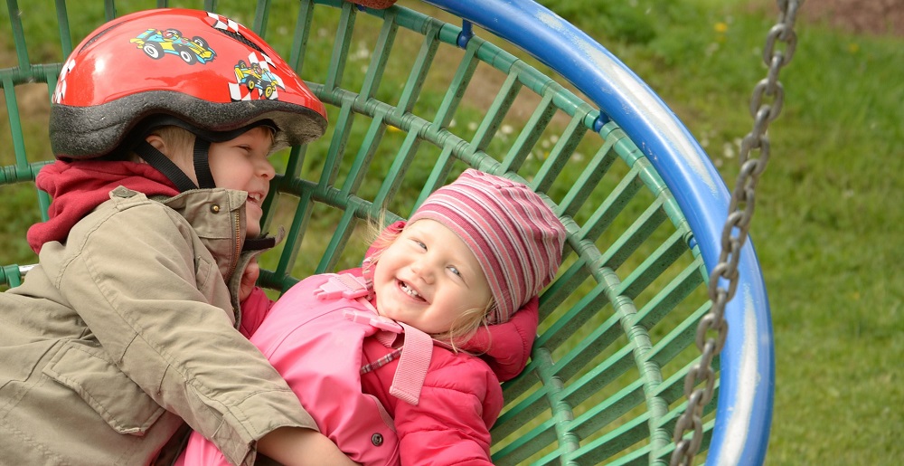 An image of two children playing on a basket swing seat.