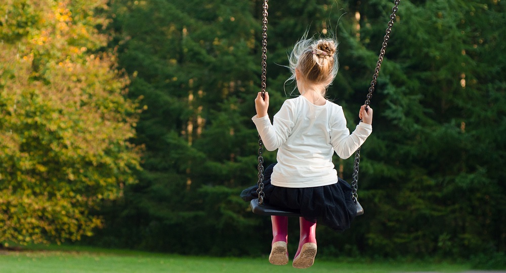 An image showing a child swinging towards a treeline.