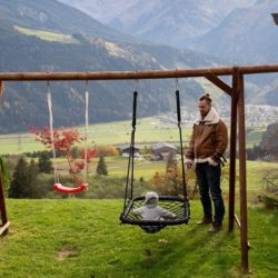 A decorative image showing a father and a son playing a playset in a backyard with a mountain view in the background.
