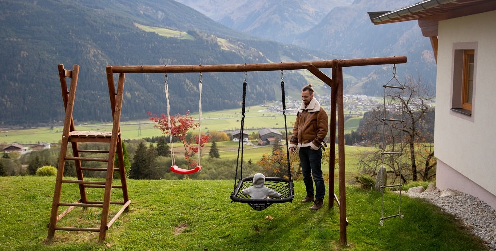 A decorative image showing a father and a son playing a playset in a backyard with a mountain view in the background.