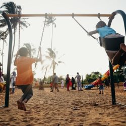An image showing children playing on a playground with palm trees in the background.
