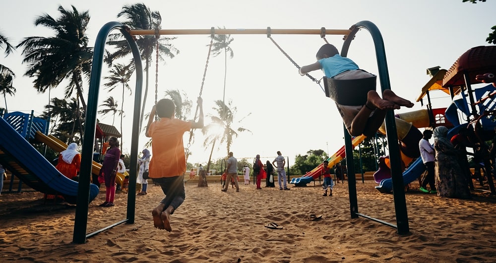 An image showing children playing on a playground with palm trees in the background.