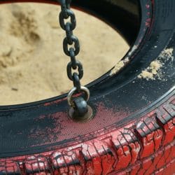An image of a black tire swing that is painted red and attached to a swing set.